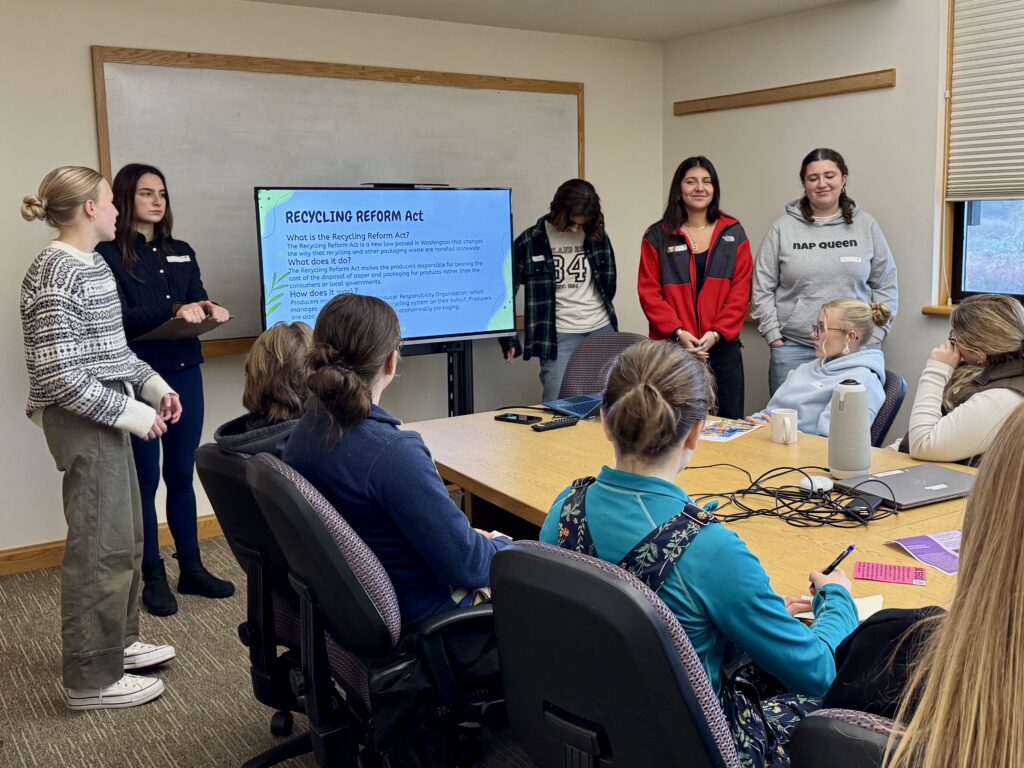 students standing in a room, doing a presentation about recycling to another group of students