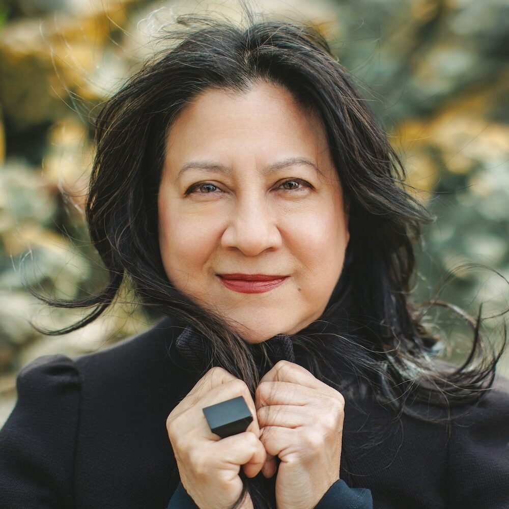 ayn wearing a black jacket and a black ring smiling