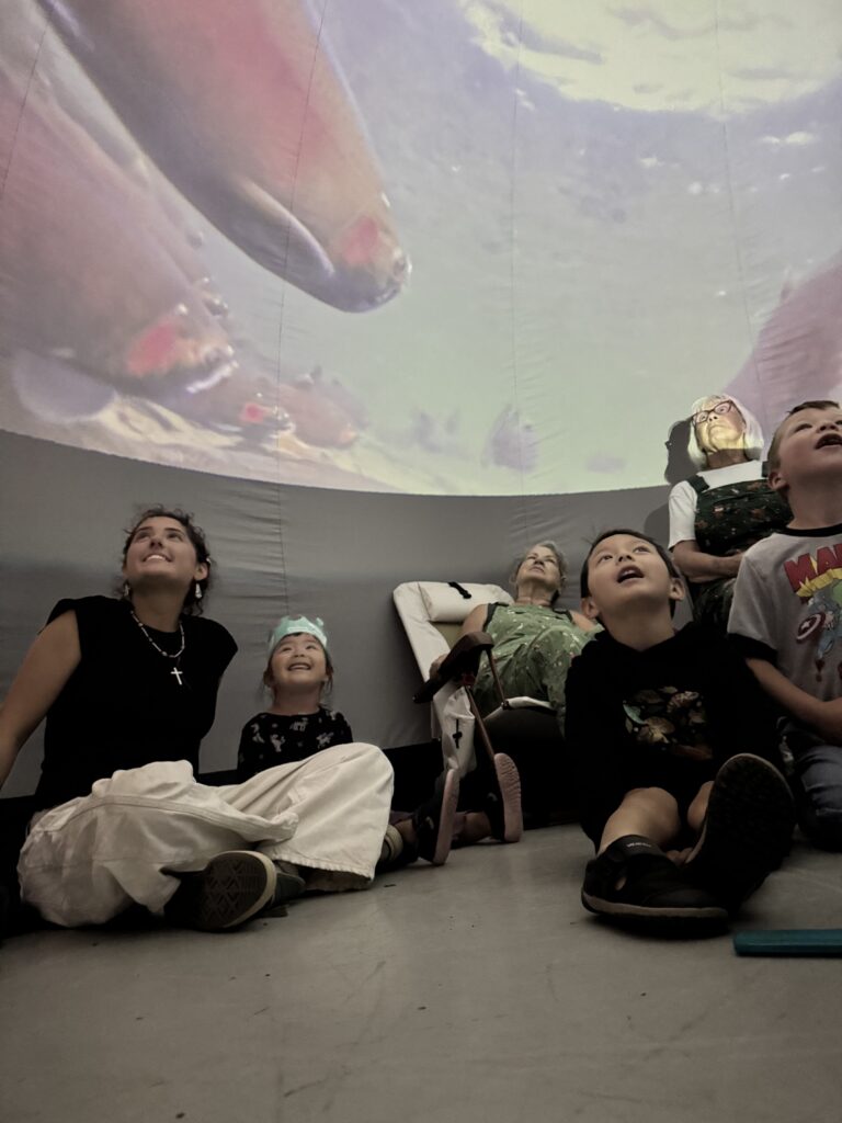 People inside the Salish Sea Dome watching an underwater video projection of salmon.